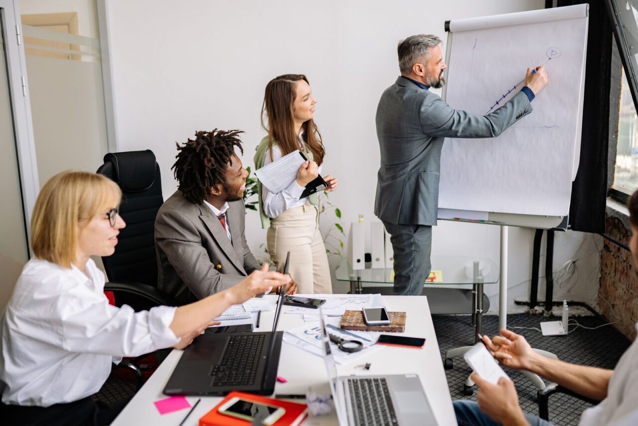Adviser leading a team session at a flipchart while colleagues take notes around a meeting table