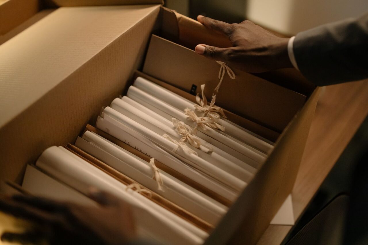 Hands in a suit sleeve placing ribbon-tied files into a cardboard archive box