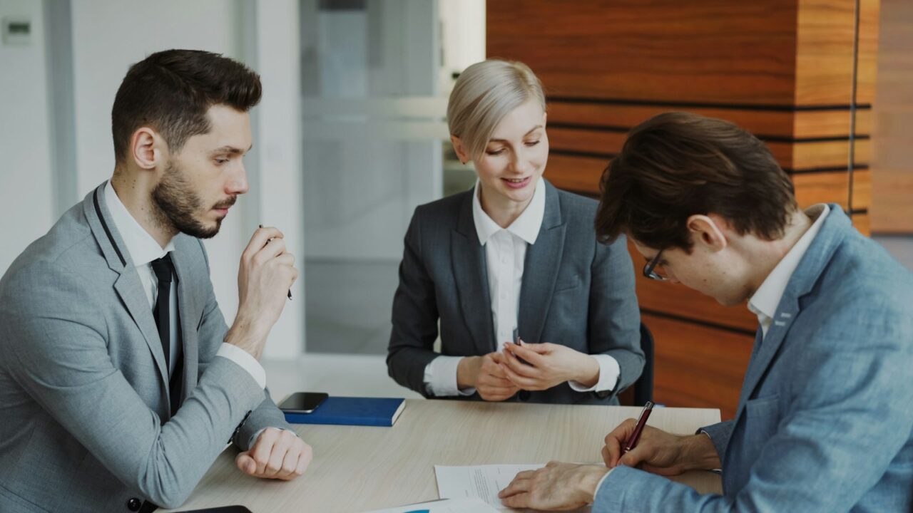 Three professionals in business suits reviewing papers together at an office table