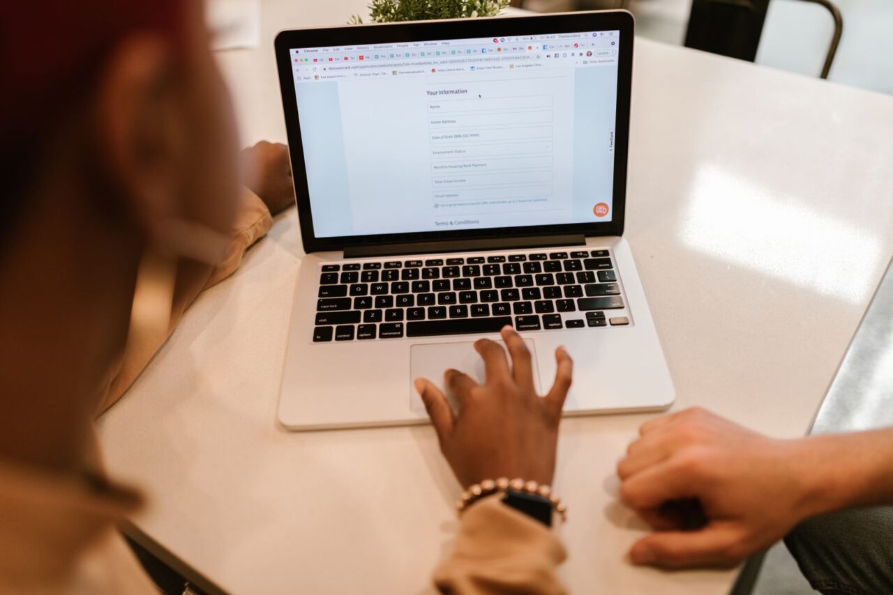 Close-up of a person completing an online form on a laptop at a white office table