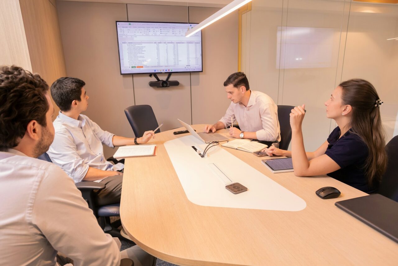Financial Due Diligence Services in Dubai — hero Four colleagues in a meeting room reviewing a spreadsheet on a wall-mounted screen, with laptops and notebooks on the table