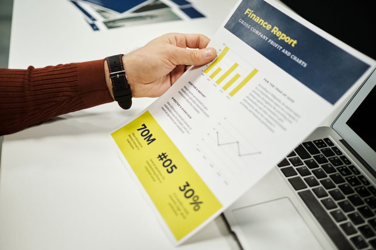 Financial Due Diligence Services in Dubai — section1 Hand holding a printed finance report with charts beside an open laptop