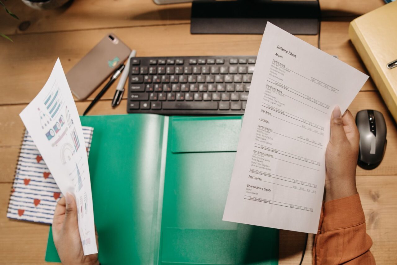 Financial Due Diligence Services in Dubai — section2 Hands holding a printed balance sheet and a chart over a desk with a keyboard and an open green folder
