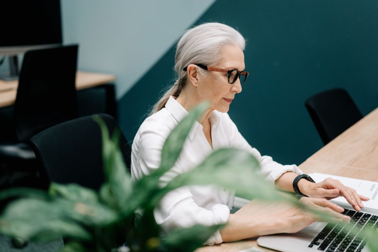 E-Invoicing in the UAE: Scope, Deadlines and Penalties — section1 Woman in a white shirt and glasses working on a laptop at a desk in a modern office