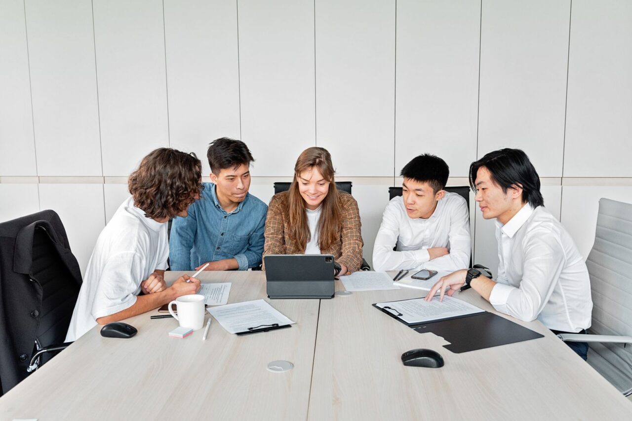 E-Invoicing in the UAE: Scope, Deadlines and Penalties — section2 Five colleagues around a meeting table reviewing a tablet and printed documents in a white office