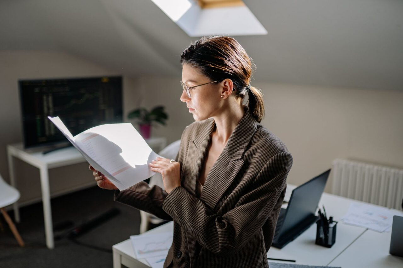 Internal Audit Services in Dubai — hero Analyst in a blazer and glasses reading a printed report beside her desk and laptop