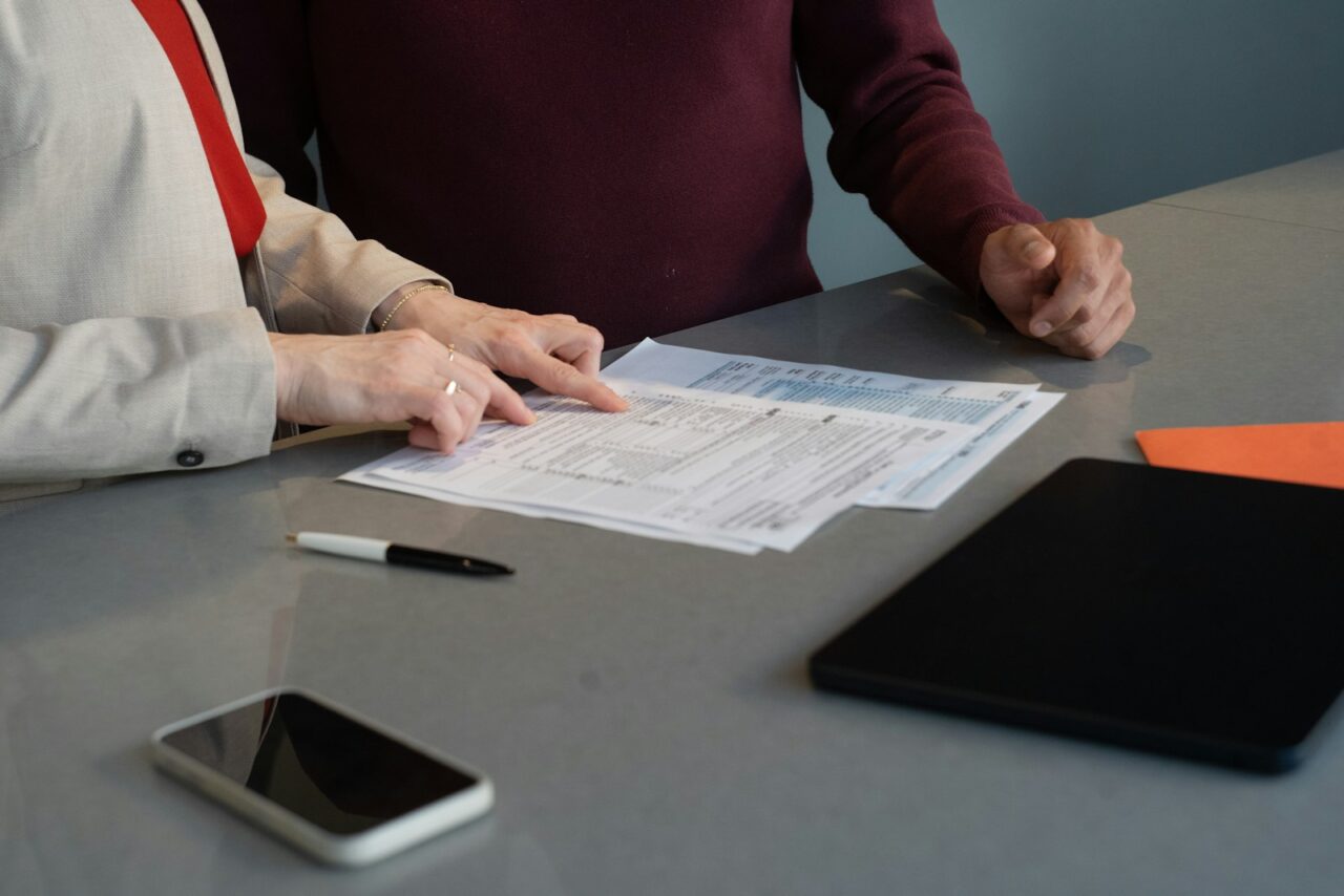 Internal Audit Services in Dubai — section1 Two people at a table going through printed forms line by line, with a pen, phone and tablet beside them