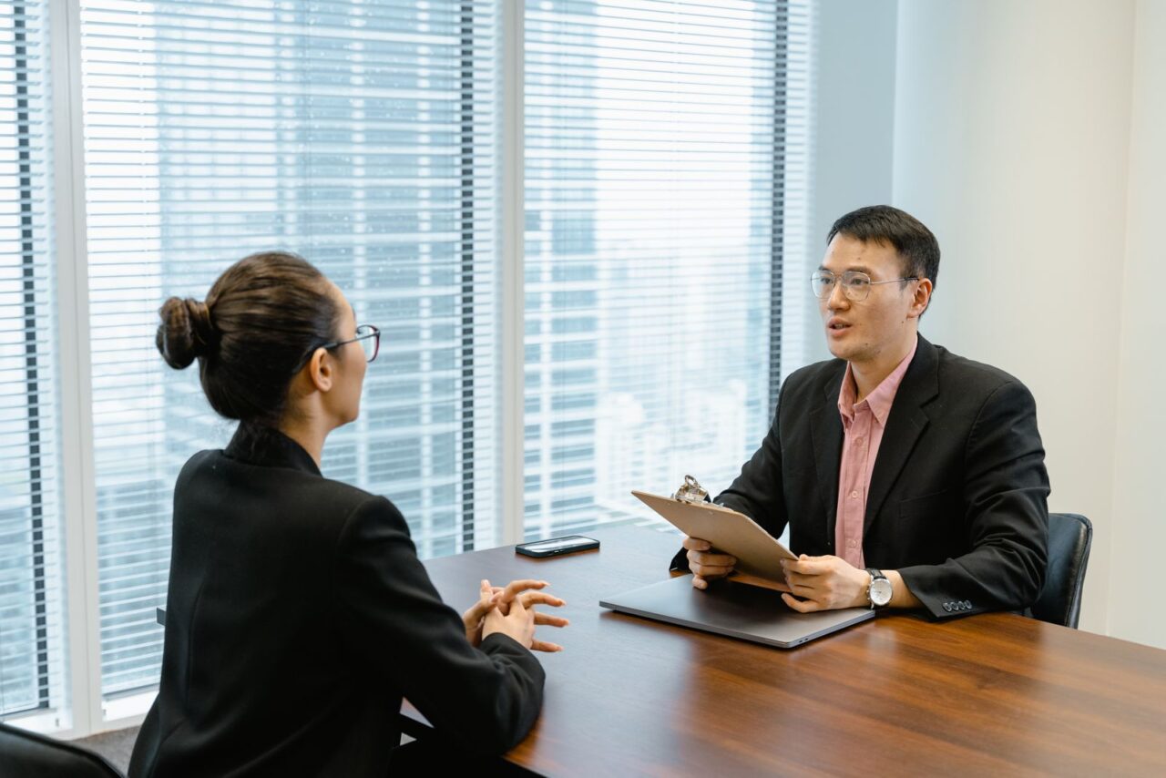 Adviser holding a clipboard in a calm meeting with a client across a table in a high-rise office