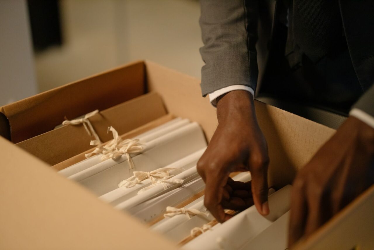 Hands in a suit sleeve packing tied bundles of business records into an archive box