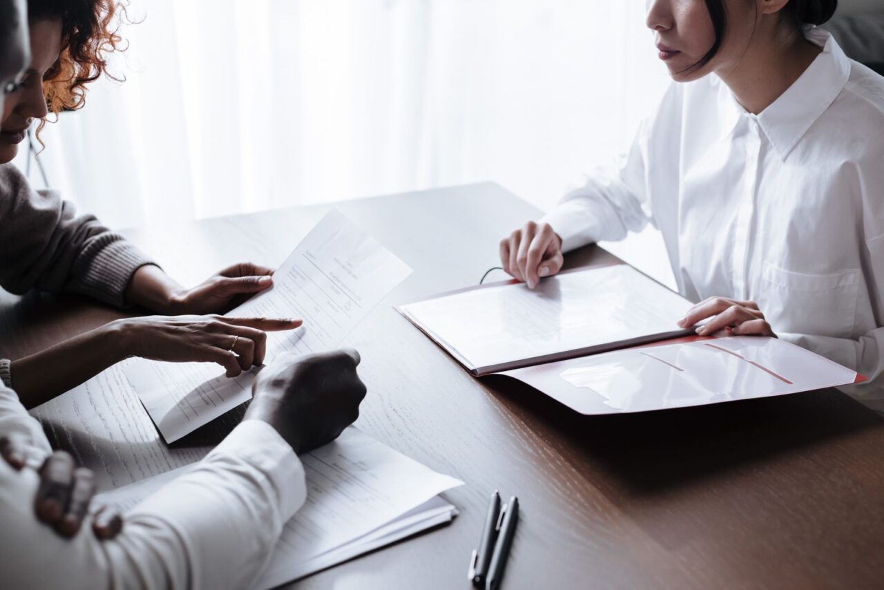 Two people at a wooden table going through printed letters and an open folder of documents together