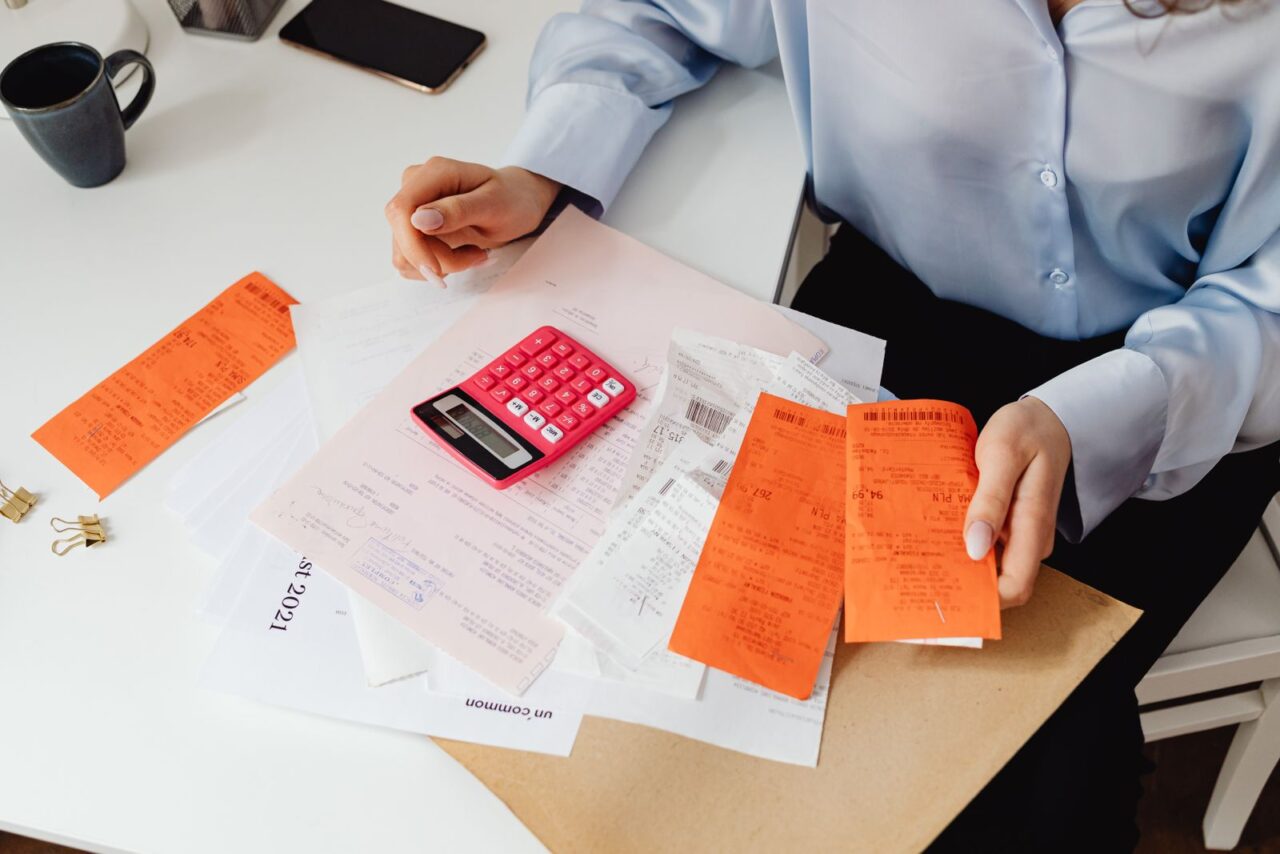 Person sorting printed receipts and invoices on a white desk next to a calculator
