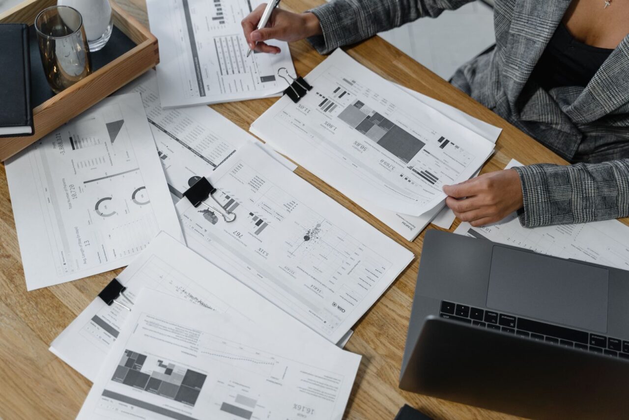 Person with a pen turning the pages of a printed financial report on a desk