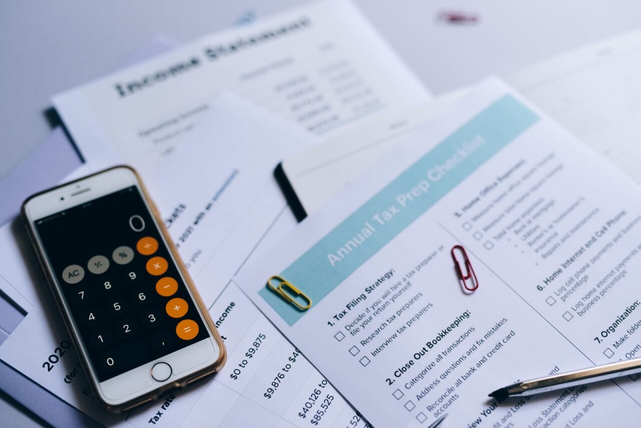 Printed tax checklist, income statement and a phone calculator spread across a desk